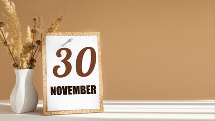 november 30. 30th day of month, calendar date.White vase with dead wood next to cork board with numbers. White-beige background with striped shadow. Concept of day of year, time planner, autumn month