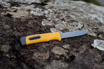A bushcraft survival knife lies on a stone, a gray natural background of moss, the fire is hidden in the handle of the knife.
