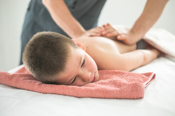 Obraz na płótnie Canvas Boy toddler relaxes from a therapeutic massage. Physiotherapist working with patient in clinic to treat the back of a child