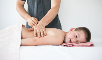 Fototapeta na wymiar Boy toddler relaxes from a therapeutic massage. Physiotherapist working with patient in clinic to treat the back of a child