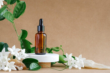 A cosmetic empty bottle with amber glass dropper on a concrete pedestal. Natural beauty products. Mineral organic oil or face serum. Skin care on beige background with white flowers and green leaves.