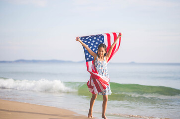 Happy kid girl playing on the beach and holding USA flag, Child girl raising United States of America flag