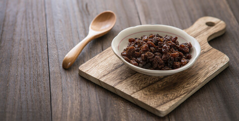 A small plate with raisins on a wooden table. Wooden spoon and dry grape on the plate.