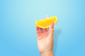 Colorful shot of raised female's hand with half of fresh orange,  posing over blue background. Hands and gesturing concept