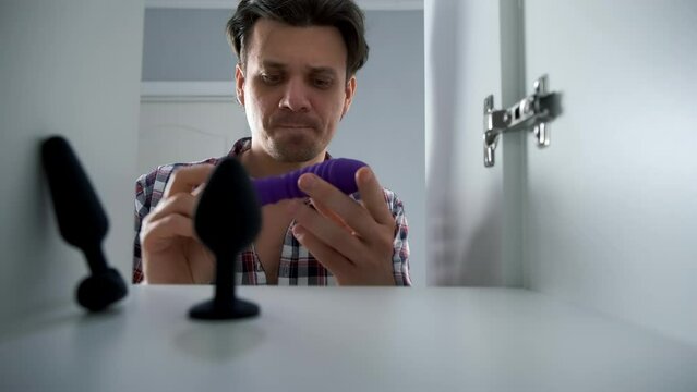 Young man is choosing sex toys opening wardrobe door at home. Using toys to get pleasure in sex. Active and diverse sex life.