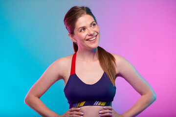 Smiling sporty woman in fitness bra sportswear with hands on waist looking up. Female fitness portrait isolated on neon multicolor background.