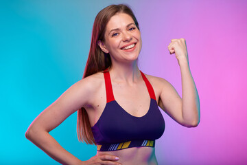 Fototapeta na wymiar Smiling sporty woman in fitness sportswear flexes arms and demonstrates muscles. Female fitness portrait isolated on neon multicolor background.