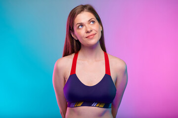 Smiling sporty woman in fitness bra sportswear with hands behind back looking up. Female fitness portrait isolated on neon colored background.
