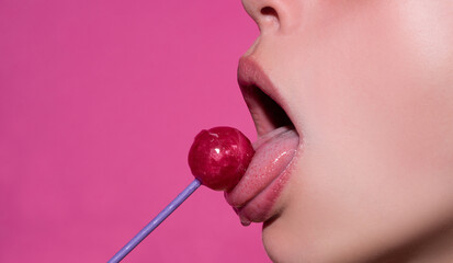 Sexy mouth licking lollipop, red female glossy lips and pink candy lollipop isolated on pink. - obrazy, fototapety, plakaty