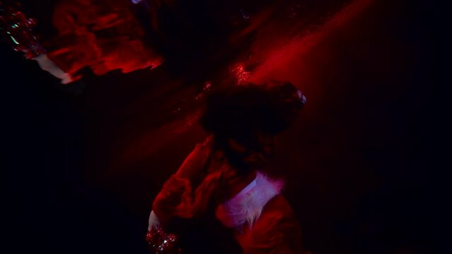 a brunette with long hair dances with tinsel in her hands in dark water and is reflected in its surface. red light. the average plan. the camera is tilted