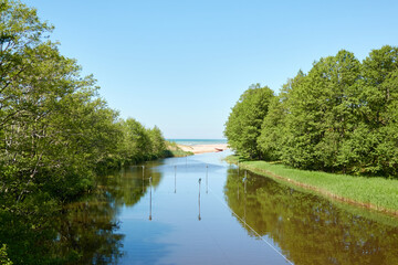 Forest river flowing into the Baltic sea. Beach, sand dunes, stones, pebbles, green trees. Clear...