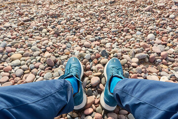 Man in a blue jeans and trekking boots. Sand and pebbles close-up. Natural textures. Baltic sea shore (beach) at sunset. Soft sunlight. Nature, ecology, tourism. hiking, wanderlust, exploring concepts
