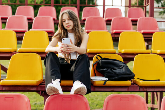 A teenage girl sits on the school bleachers and writes a message on her phone in her free time
