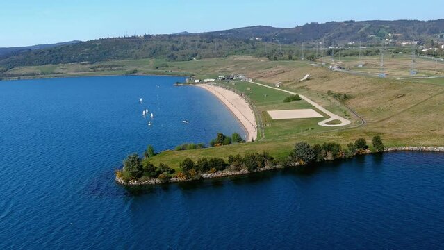 large lake with garden for walking, beach and sunbathing area with lawn where sailing classes are taught, sunny day. Drone shot orbits to the left. As Pontes, Lugo, Spain