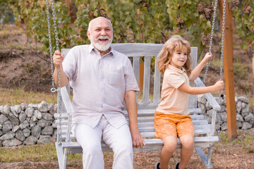 Grandfather and son swinging in garden. Granddad and grandchild playing on swing.