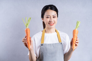 Young Asian woman holding vegetables on background