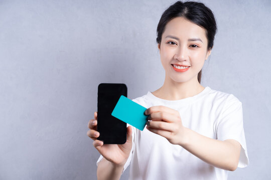 Image of young Asian woman holding bank card on background