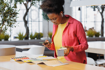 African American woman architect or designer works in a coworking office. a woman creates a residential house project and holds a mock-up of a house in her hands. african american engineering student