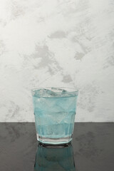 Blue refreshing summer drink. Iced cocktail on grey textured background. Vertical orientation, copy space