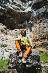 A climber sits on a cliff, mountain hiking, a trip to the mountains, a sporty person, a guy smiling, outdoor recreation, a traveler's smile.