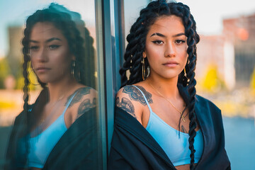 Urban session. Young woman of black ethnicity with long braids and with tattoos, glass, looking