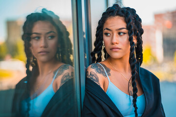 Urban session. Young woman of black ethnicity with long braids and with tattoos, glass, looking