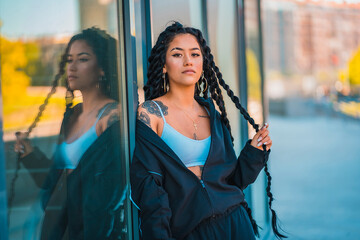 Urban session. Young woman of black ethnicity with long braids and with tattoos, in some windows