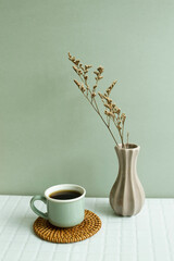 Cup of coffee and dry flowers on white table. khaki green wall background
