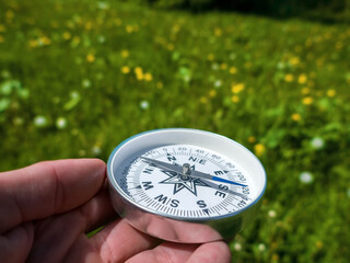 A compass in person's hand in park with flowers. Orient yourself in current situation (urban...