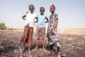 Three African girls standing together on an arid field somewhere in the outskirts of an rural...