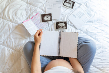 Obraz premium Pregnant woman list. Young pregnancy mother holding notepad. Pregnant lady writing check list of baby. Pregnancy, maternity, healthcare concept.
