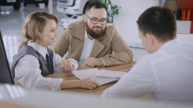 A married couple signs a contract for the sale of a new car. The manager shakes hands and congratulates by handing over the keys.