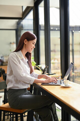 Side view young female freelancer sitting at wooden counter in coffee shop and using laptop computer