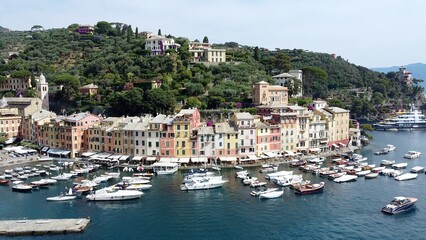 Fototapeta na wymiar Europe, Italy , Portofino, Liguria - Drone aerial view of Portofino harbor with typical colored houses - boats and amazing sea bay surrounded by nature in Portofino natural park - Tourist attraction 