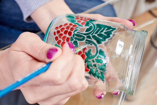 A girl paints a glass jar with stained glass paints