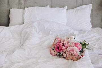 Close up shot of a gorgeous bouquet of peonies and ranunculus flowers on the empty unmade bed with...