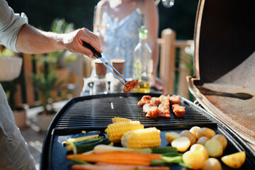 Unrecognizable man grilling ribs and vegetable on grill during family summer garden party, close-up