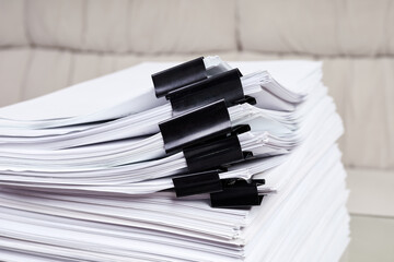 A stack of office papers, some of which are fastened with black binders