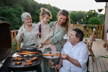 Multi generation family grilling outside on patio in summer during garden party
