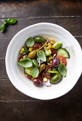 Simple Salad with Green and Kalamata Olives, Cucumber, Cherry and marinated Tomatoes, Capers and Jalapeno Pepper. Brown wooden background. Top view.  