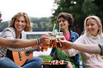 Group of multiracial young friends camping near lake, having barbecue and toasting with coctail drinks.