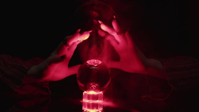 Woman sorceress using magic crystal ball for spell making witchcraft movements with hands close up.