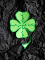 Four leaf clover on background from black crumpled craft paper with copy space and selective focus....