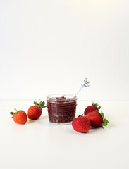 Homemade strawberry preserves or jam in a mason jar surrounded by fresh organic strawberries. Selective focus with white background.
