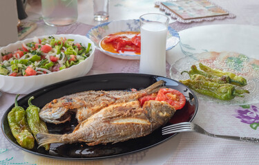 Two deep-fried sea bream, tomatoes, peppers in a black plate. Turkish raki in a glass.