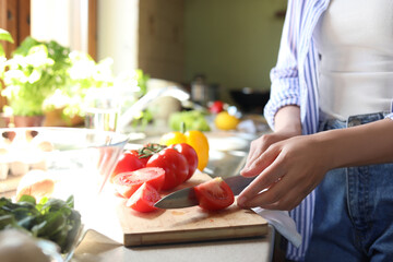 Obraz na płótnie Canvas Woman cutting fresh tomatoes at countertop in kitchen, closeup