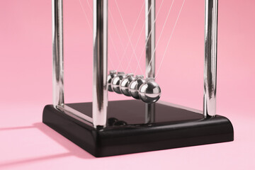 Newton's cradle on pink background, closeup. Physics law of energy conservation