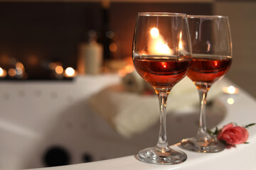 Wine in glasses and rose on edge of bath indoors. Romantic atmosphere