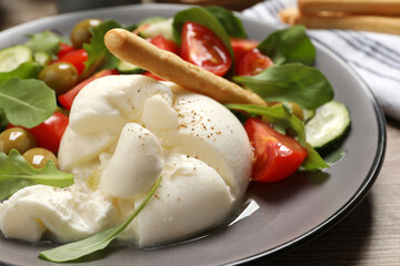 Delicious burrata salad served on wooden table, closeup