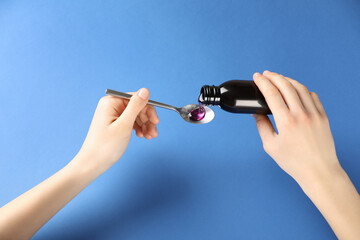 Woman pouring cough syrup into spoon on blue background, closeup